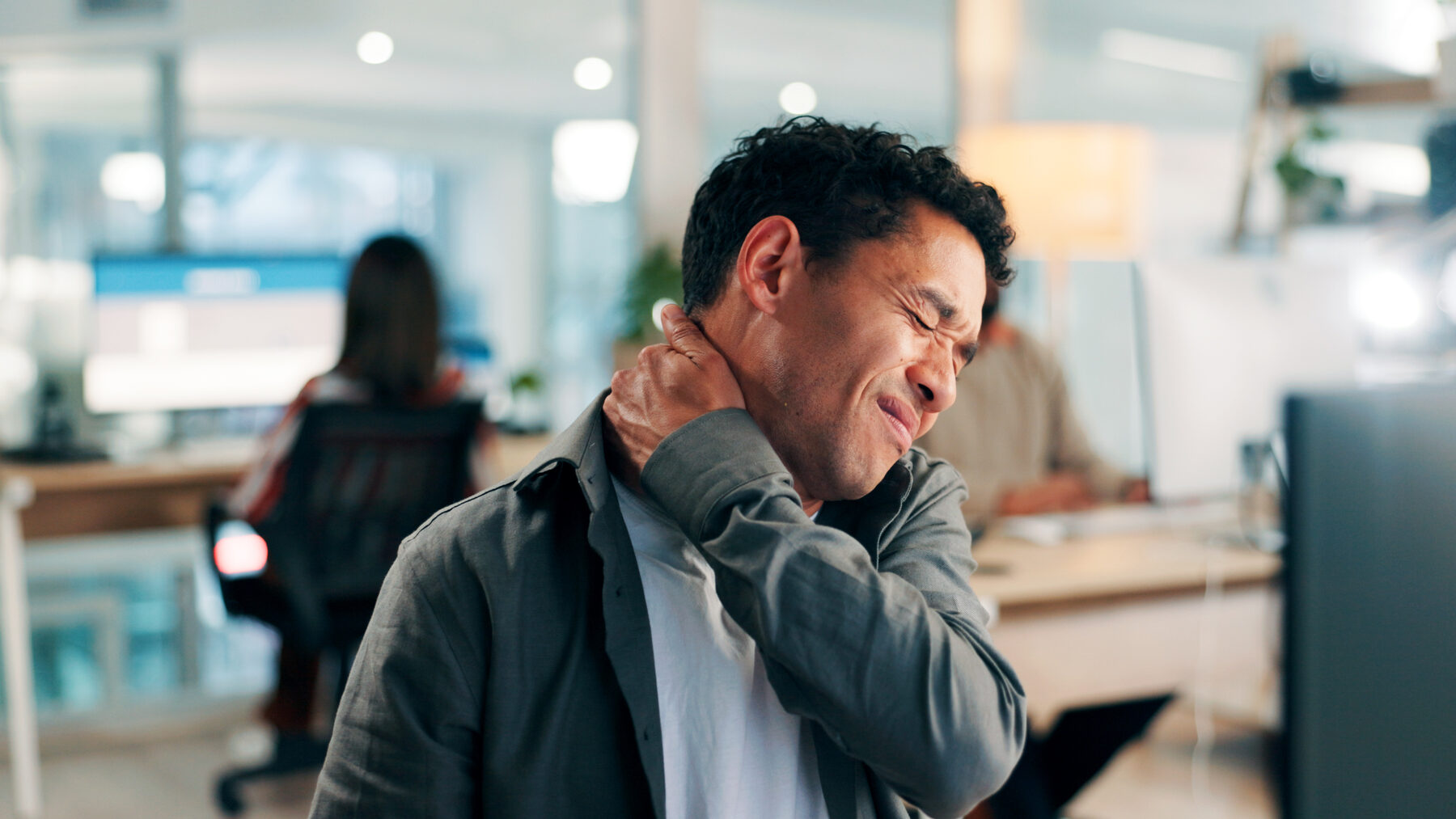 A man at a desk holding his neck in pain from office syndrome